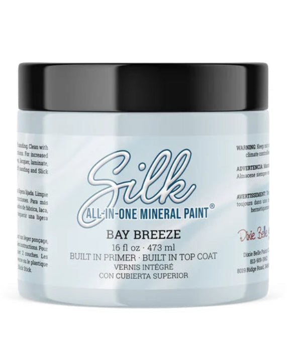 A jar of Silk All-In-One Mineral Paint in the shade Bay Breeze, featuring a light blue-gray container with a black lid and white text.