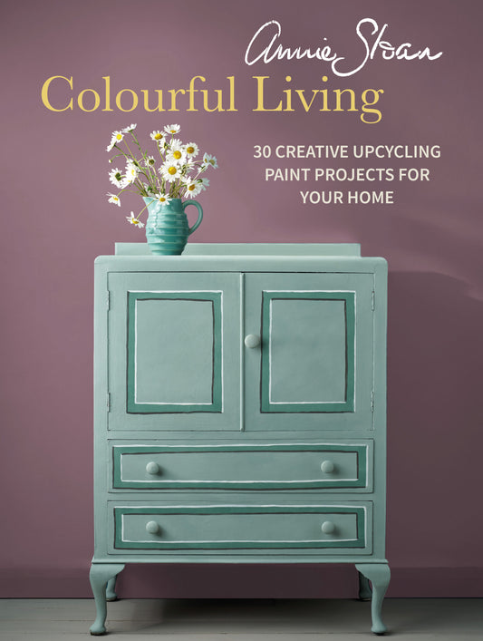 Book cover of 'Colourful Living' by Annie Sloan with a painted cabinet and flowers on a purple background