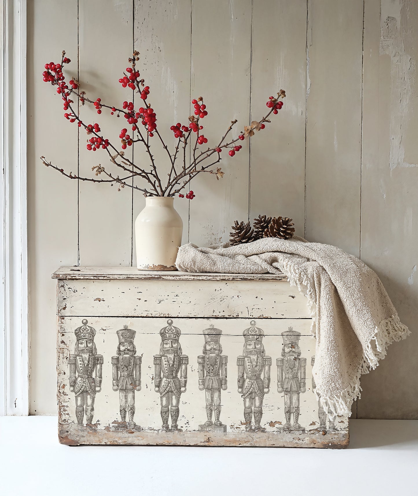 Decorative chest with nutcracker design using Iron Orchid Design Stamps, white vase with red branches, and beige blanket against a wooden wall.