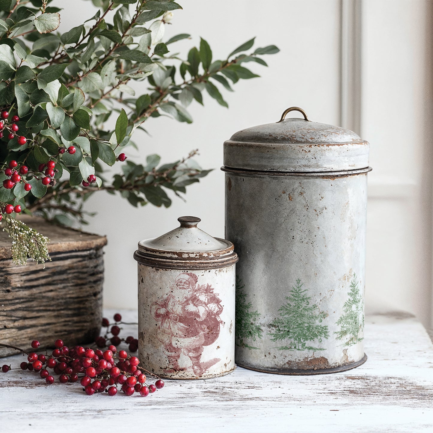 Two vintage-style metal canisters with decorative lids on a wooden surface with greenery and berries using IOD Stamps