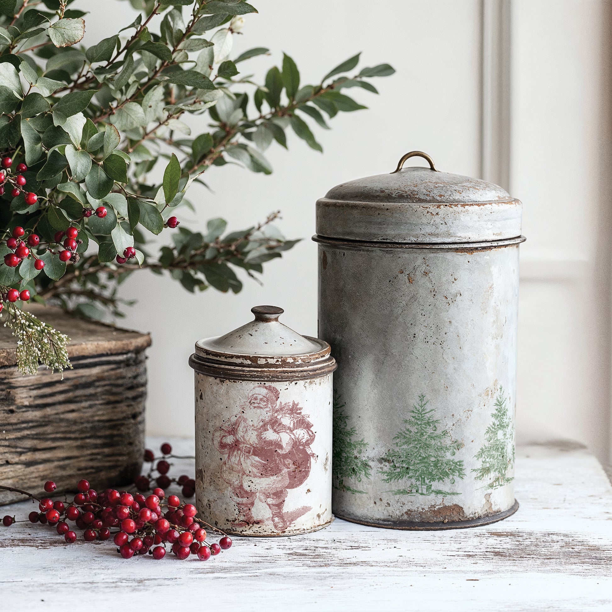 Two vintage-style metal canisters with decorative lids on a wooden surface with greenery and berries using IOD Stamps