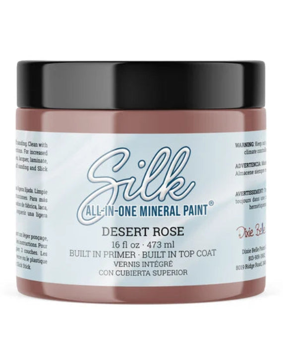 A jar of Silk All-In-One Mineral Paint in the shade Desert Rose, featuring a dusty rose-colored paint visible through the clear jar, a black lid, and a white label with blue and red text.