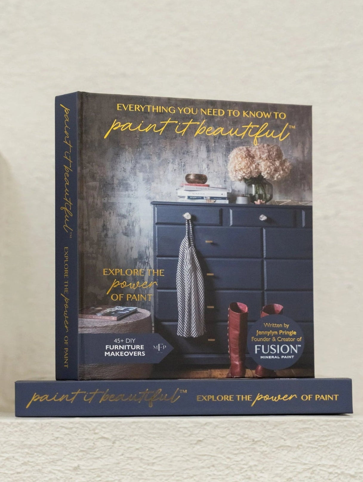 Book titled 'Everything You Need to Know to Paint It Beautiful' by Fusion Mineral Paint on a textured wall.