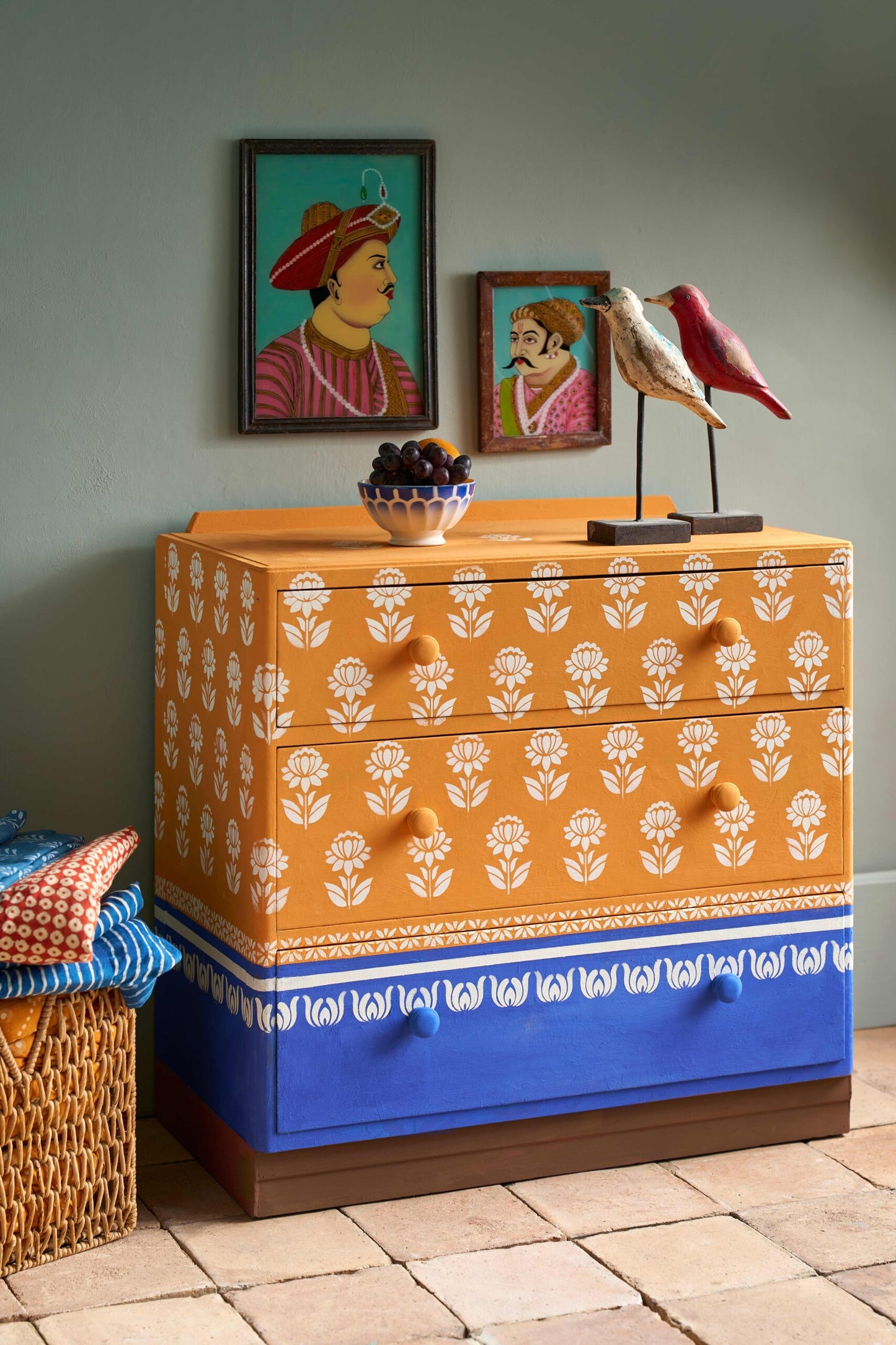 Decorative dresser with orange and blue design in a room with framed art on the wall.