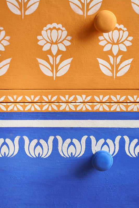 Close-up of a wooden drawer with white floral patterns on an orange and blue background.