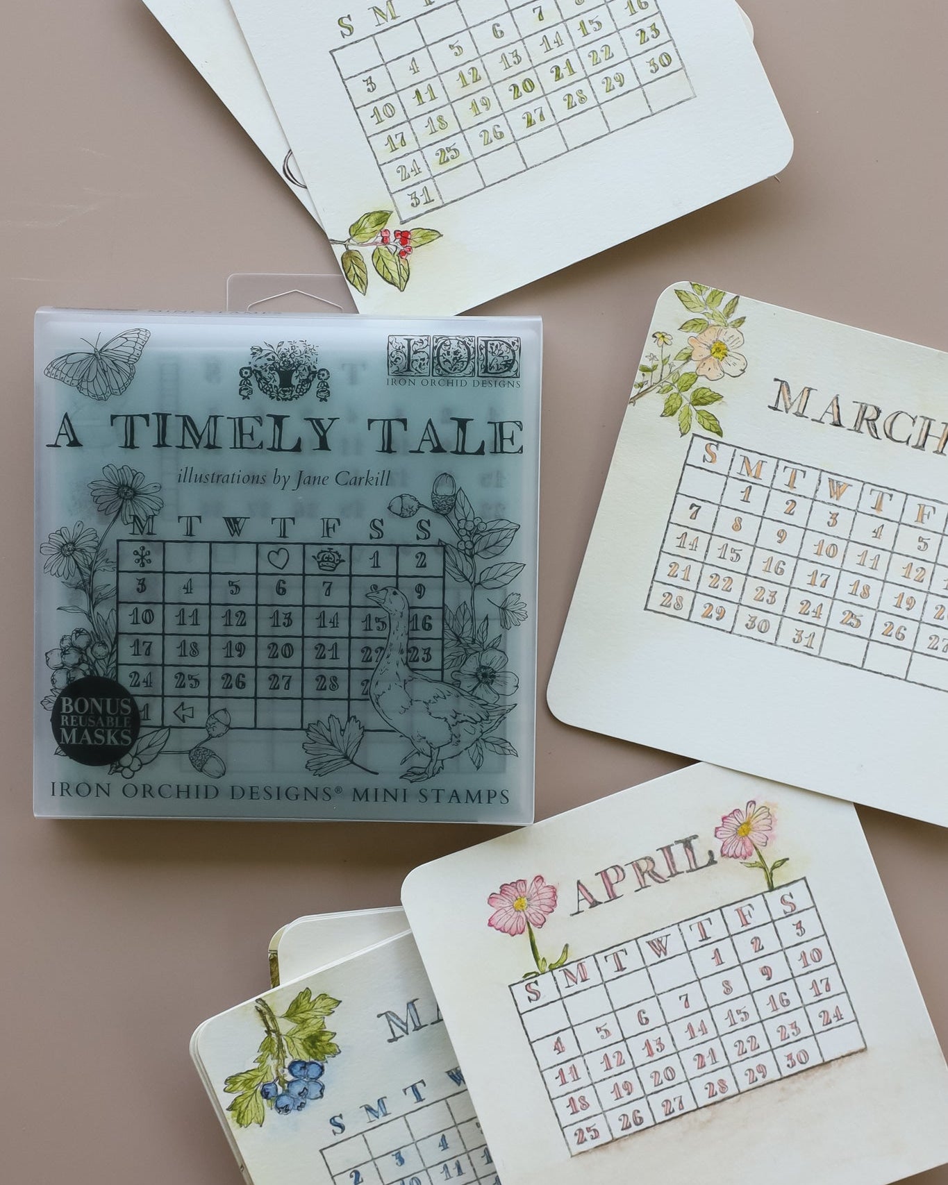 A set of illustrated monthly calendar cards with dates and days of the week, arranged around a clear plastic case labeled 'A TIMELY TALE' and 'Iron Orchid Designs Mini Stamps' on a beige background.